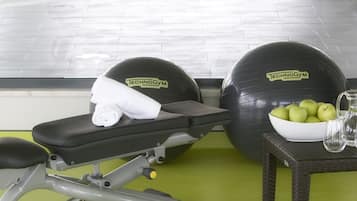 Ein Fitnessraum mit Trainingsgeräten, einem Schwimmbad und einem Korbtisch mit Äpfeln und einem Glas.
