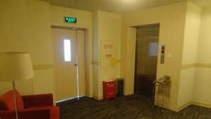 A hotel lobby with a red chair, an exit sign, an elevator, and a trash bin. - Jinjiang Inn Putian Wenxian Road E. (Putian)