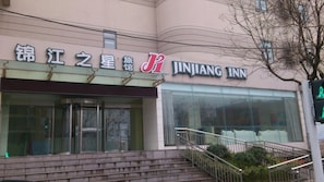 Ein Gebäude mit einem Schild für JINJIANG INN. Vor dem Eingang führen Treppen hinauf, und rechts ist ein Baum zu sehen.