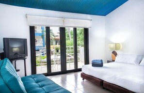 A hotel room with a bed, a television, a sofa, a lamp, and a view of the outside.