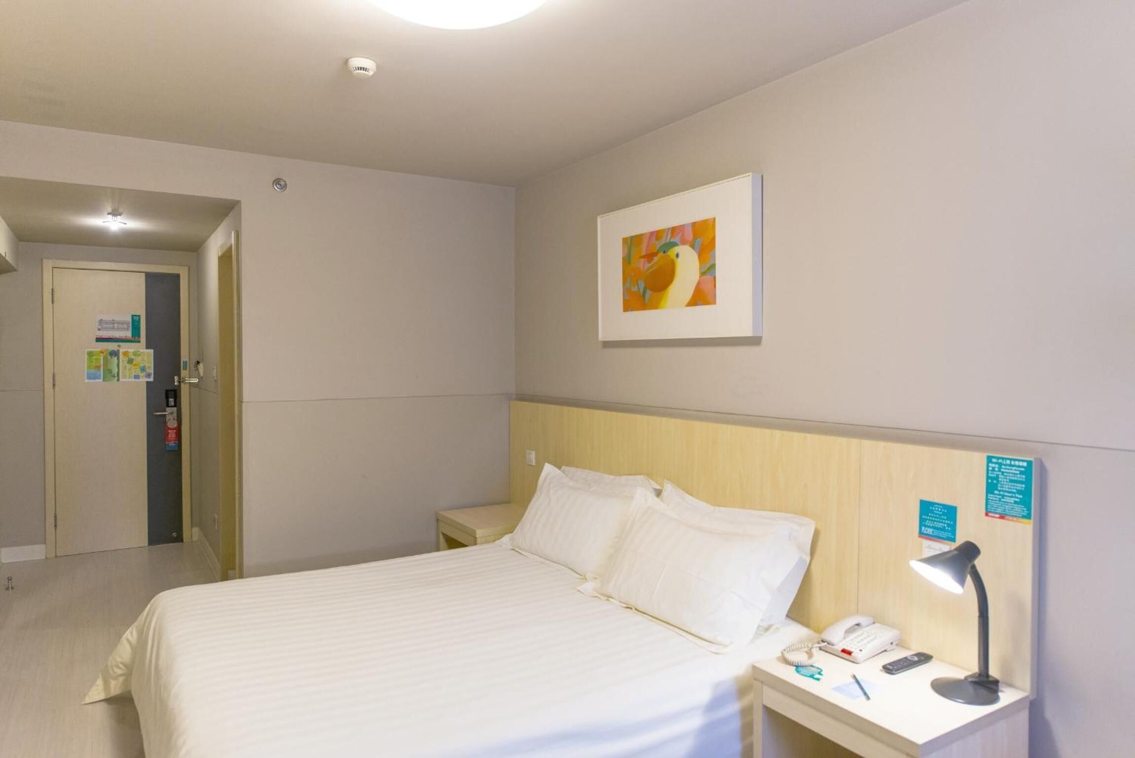 A hotel room with a bed, bedside table, lamp, and a painting on the wall.