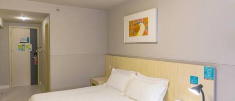 A hotel room with a bed, bedside table, lamp, and a painting on the wall.