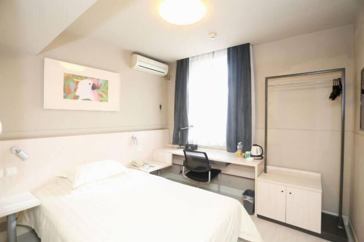 A hotel room with a bed, desk, chair, and a wardrobe.