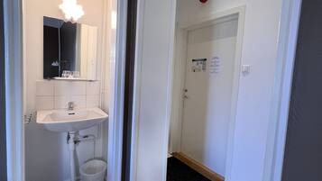 A bathroom with a white sink, mirror, and a trash bin.