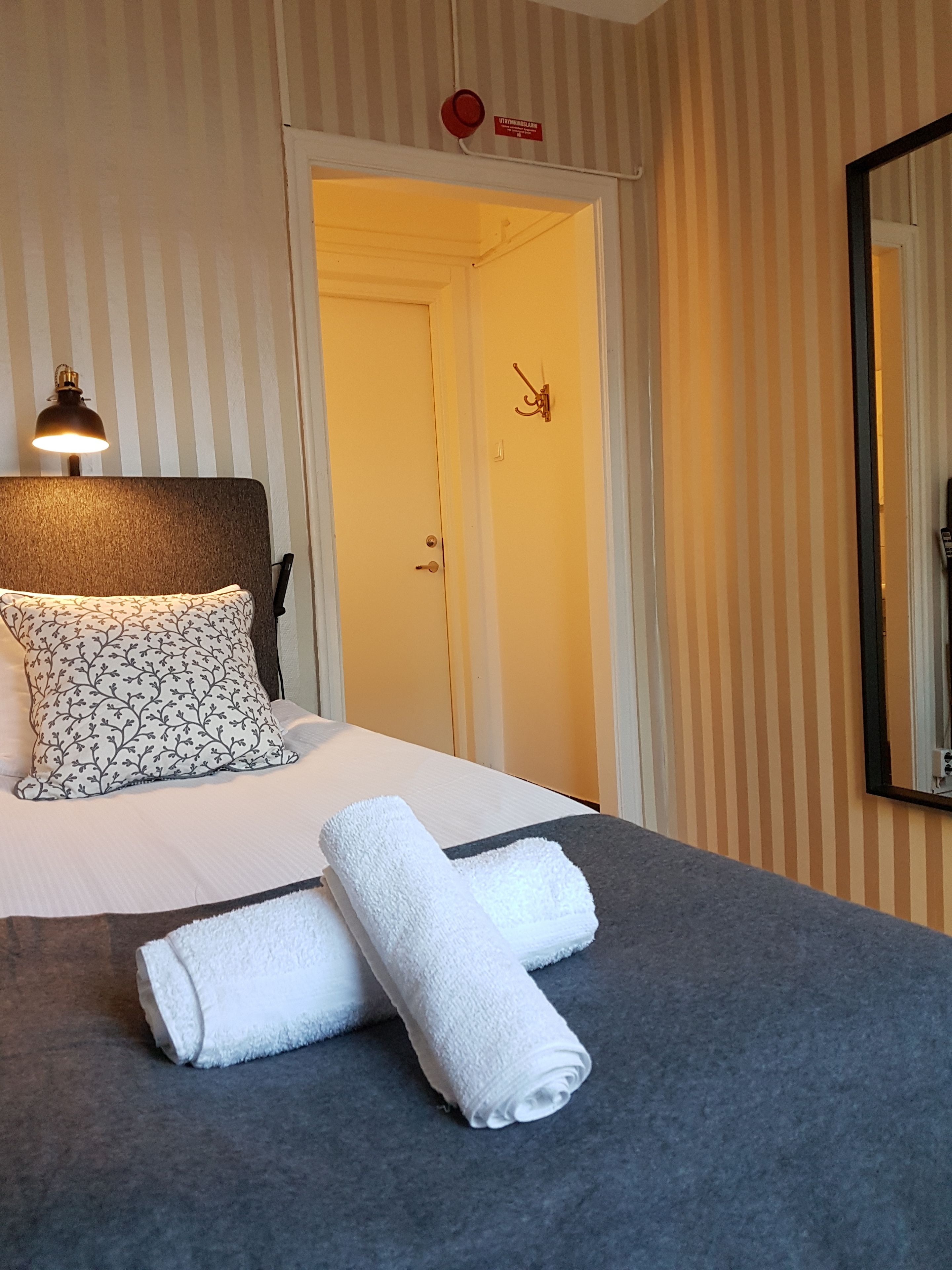 Una habitación de hotel con una cama, una lámpara de noche, una puerta y un espejo en la pared.