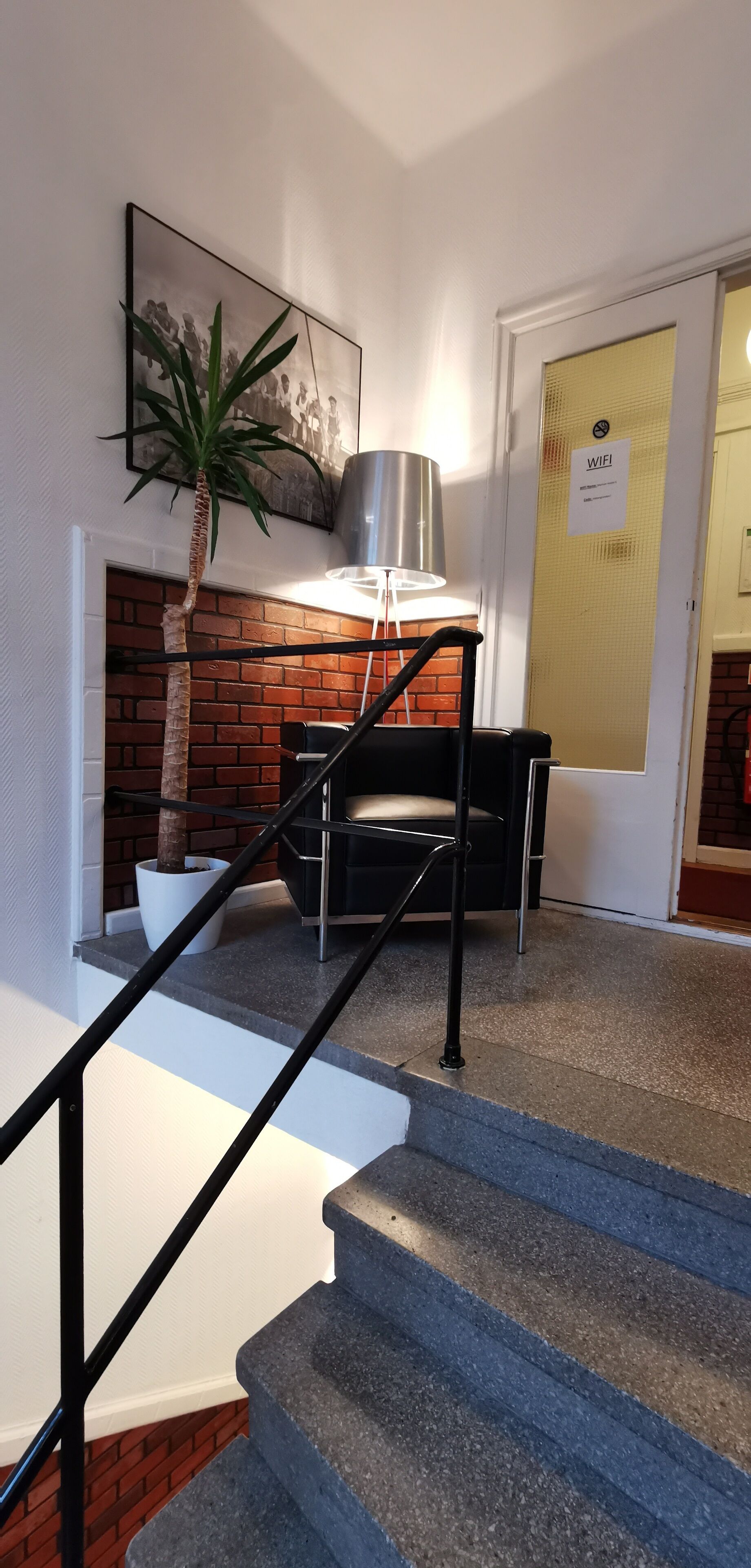Una escalera con barandilla negra, una planta en maceta, una lámpara y una puerta con un cartel de 'WiFi'.