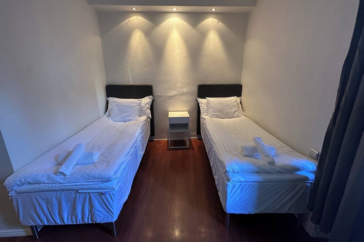 A hotel room with two single beds, a nightstand, and a small table.