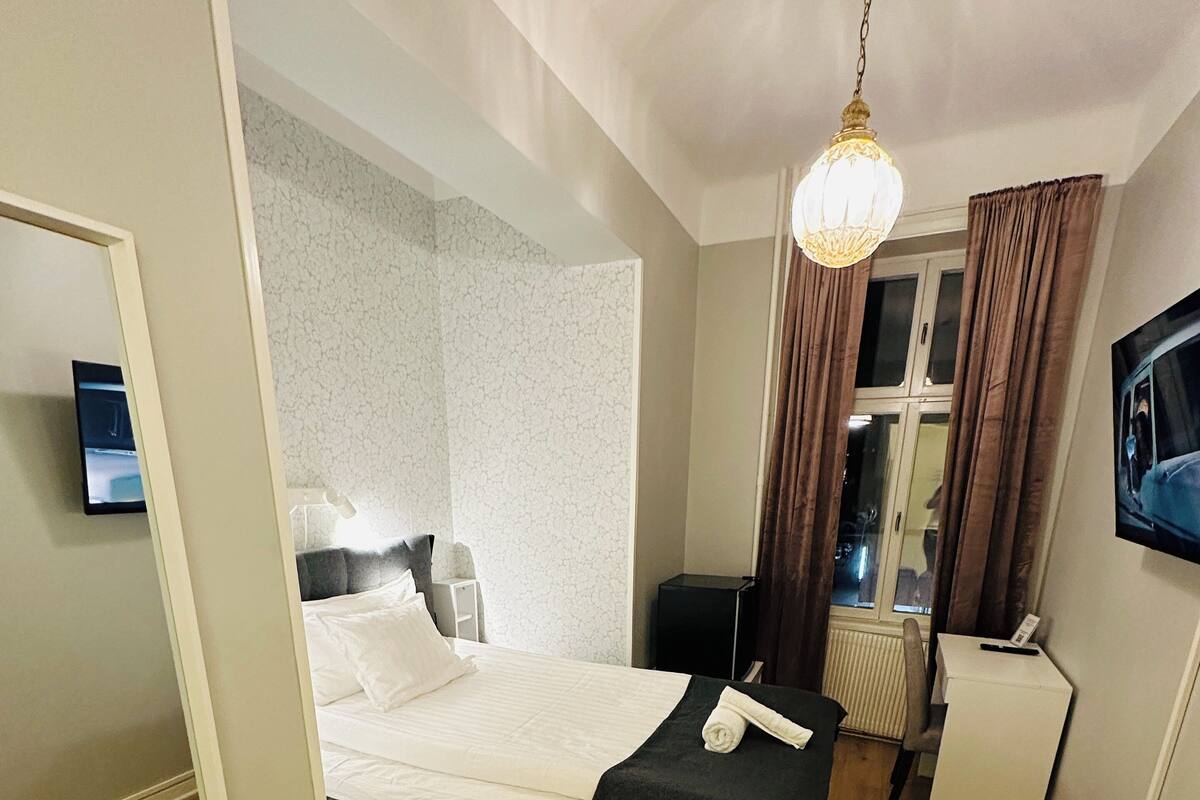 A hotel room with a bed, a desk, a chair, a TV, and a window with curtains.