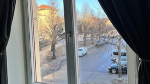 Una ventana con vista a una calle, un edificio de techo rojo y árboles desprovistos de hojas.
