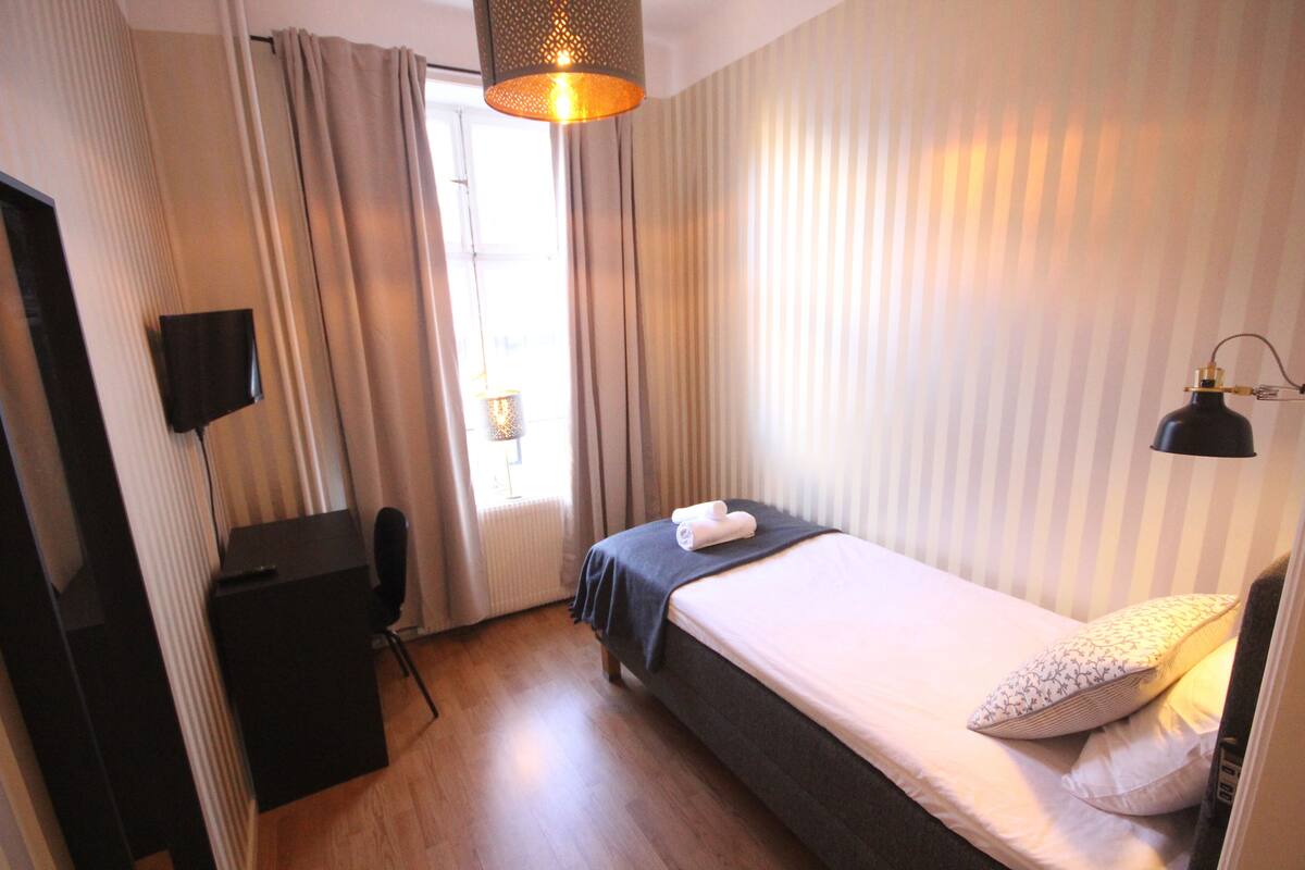 A small, neatly arranged bedroom with a bed, a desk, and a TV.