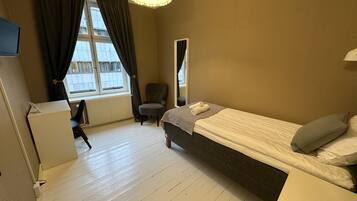 A bedroom with a bed, a desk, a chair, and a window with curtains.