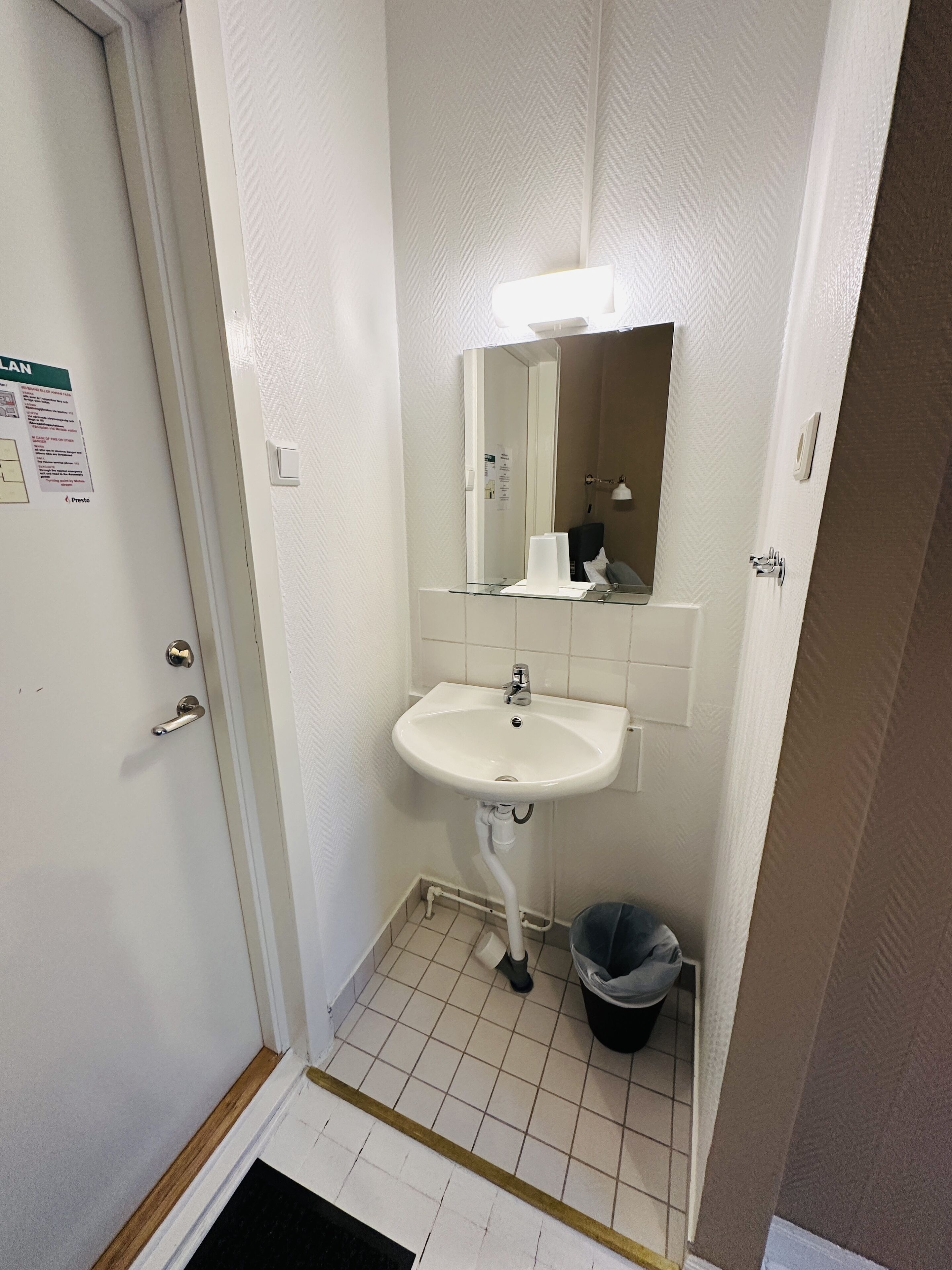 Un baño pequeño y limpio con lavamanos, espejo e instalación de cerámica.