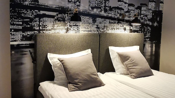 Un dormitorio con una cama grande, dos almohadas, una mesita de noche y un mural con vista a la ciudad.