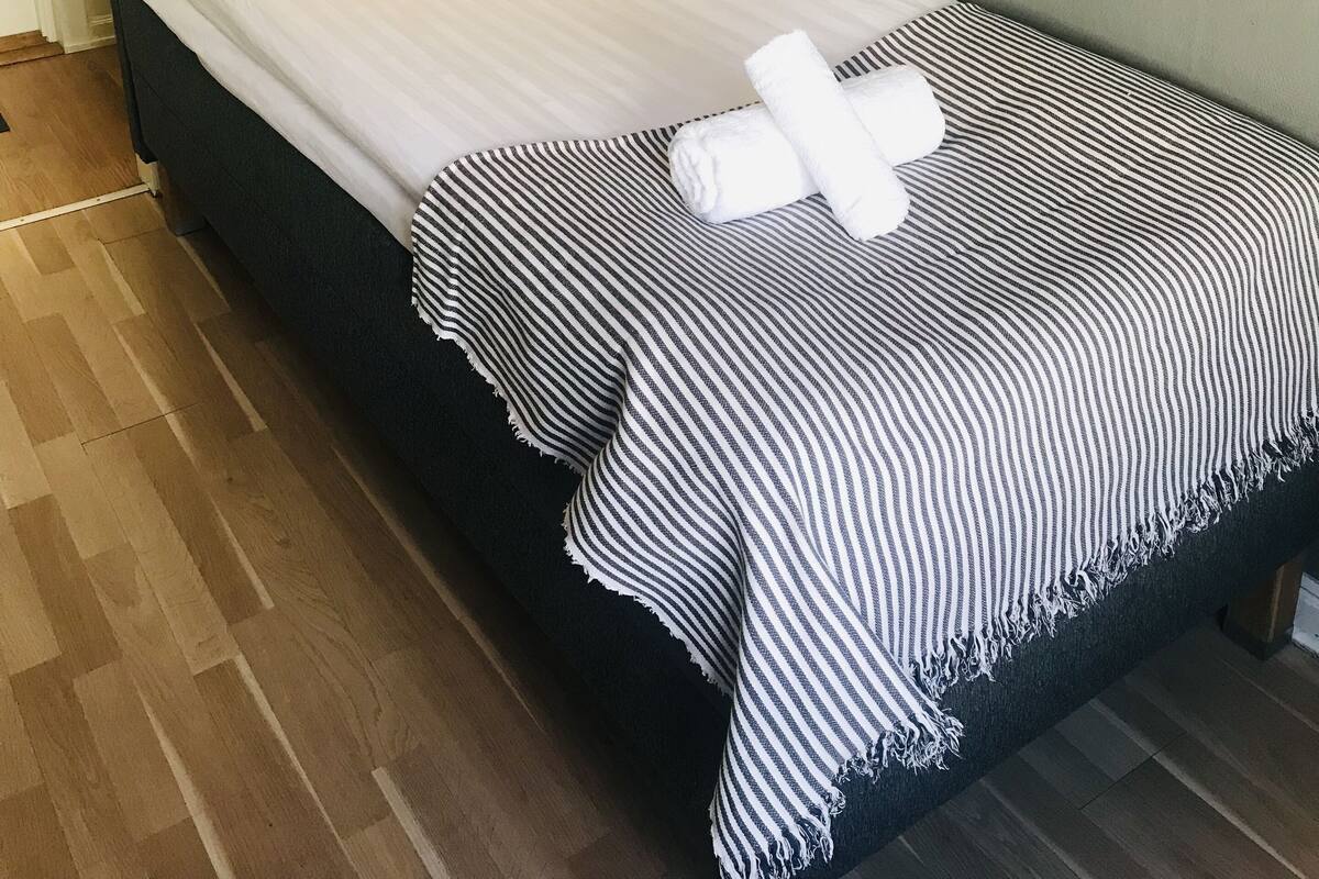 A single bed with a striped blanket, a headboard with a control panel, and a bedside table with a lamp.