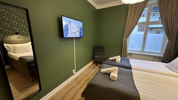 Quarto de hotel com duas camas, televisão fixada na parede, uma cadeira e janela com cortinas.