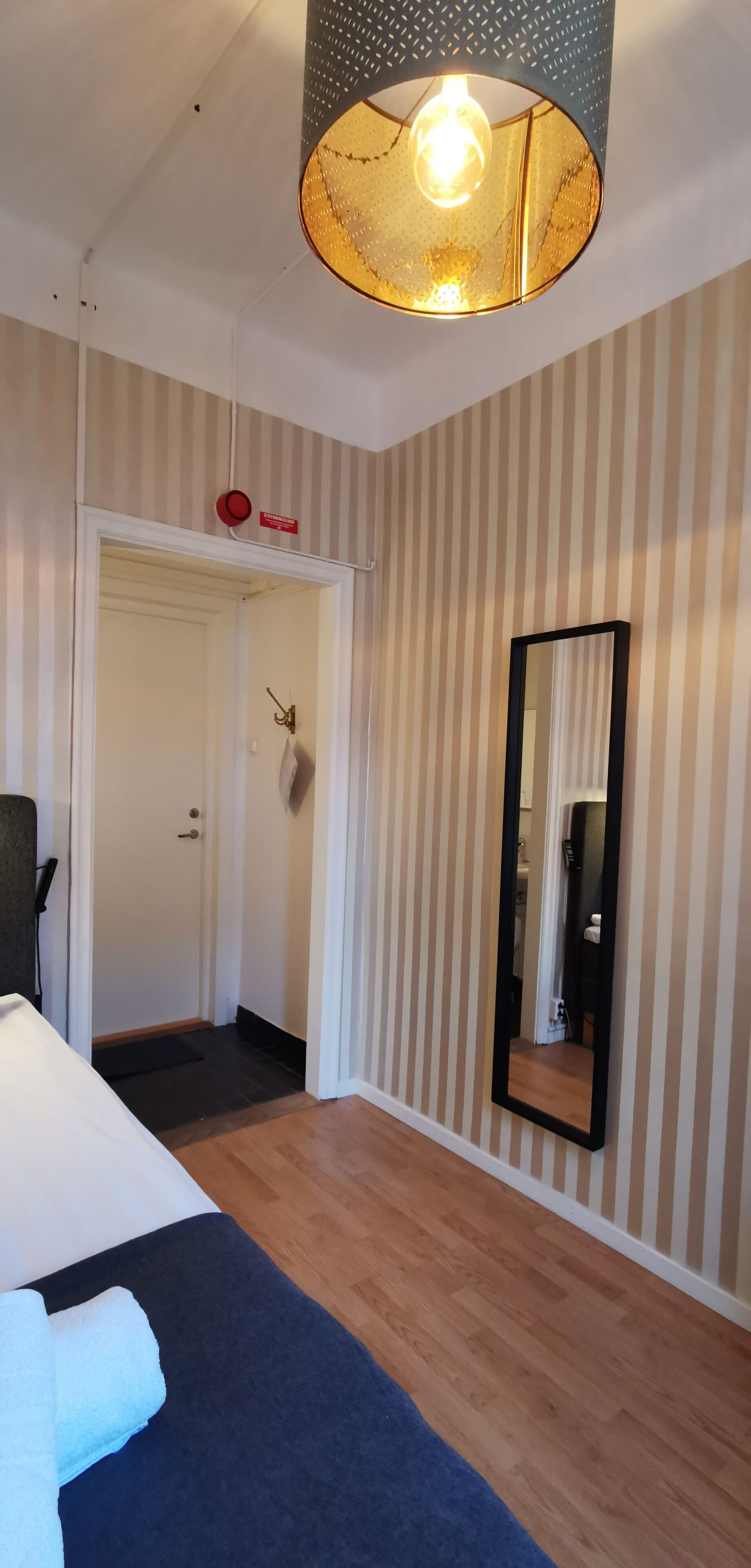 Habitación de hotel con cama, espejo, puerta y pared a rayas.