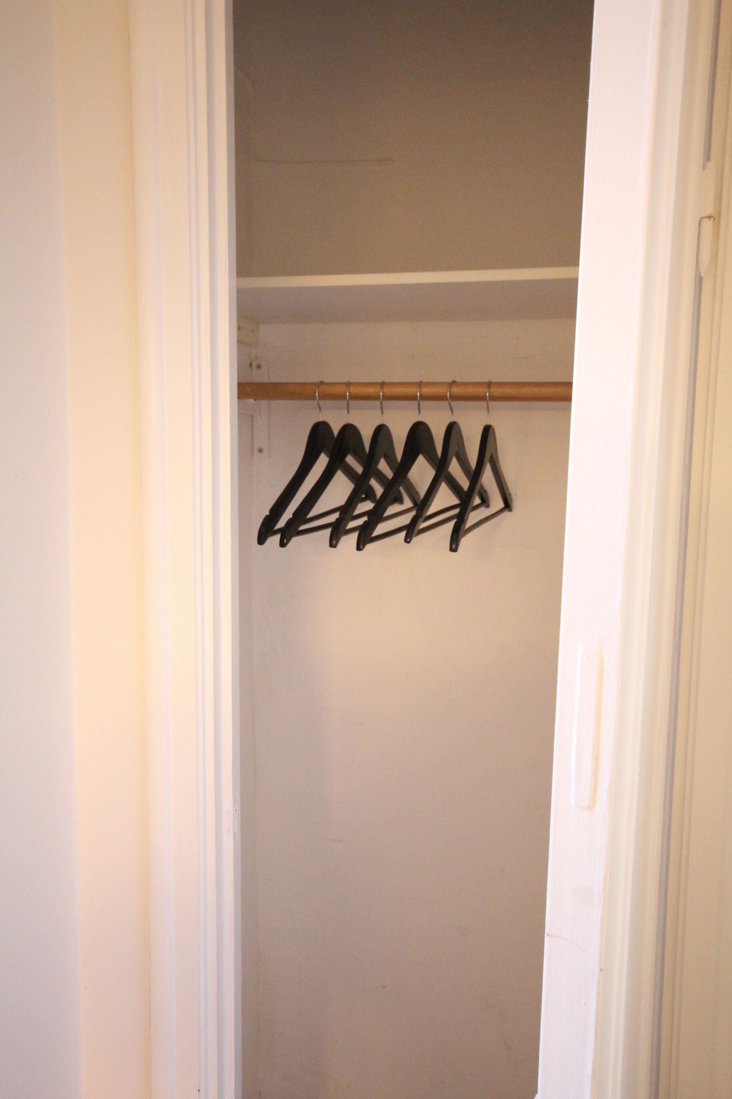 Een kast met een houten stang en zwarte ophangers.