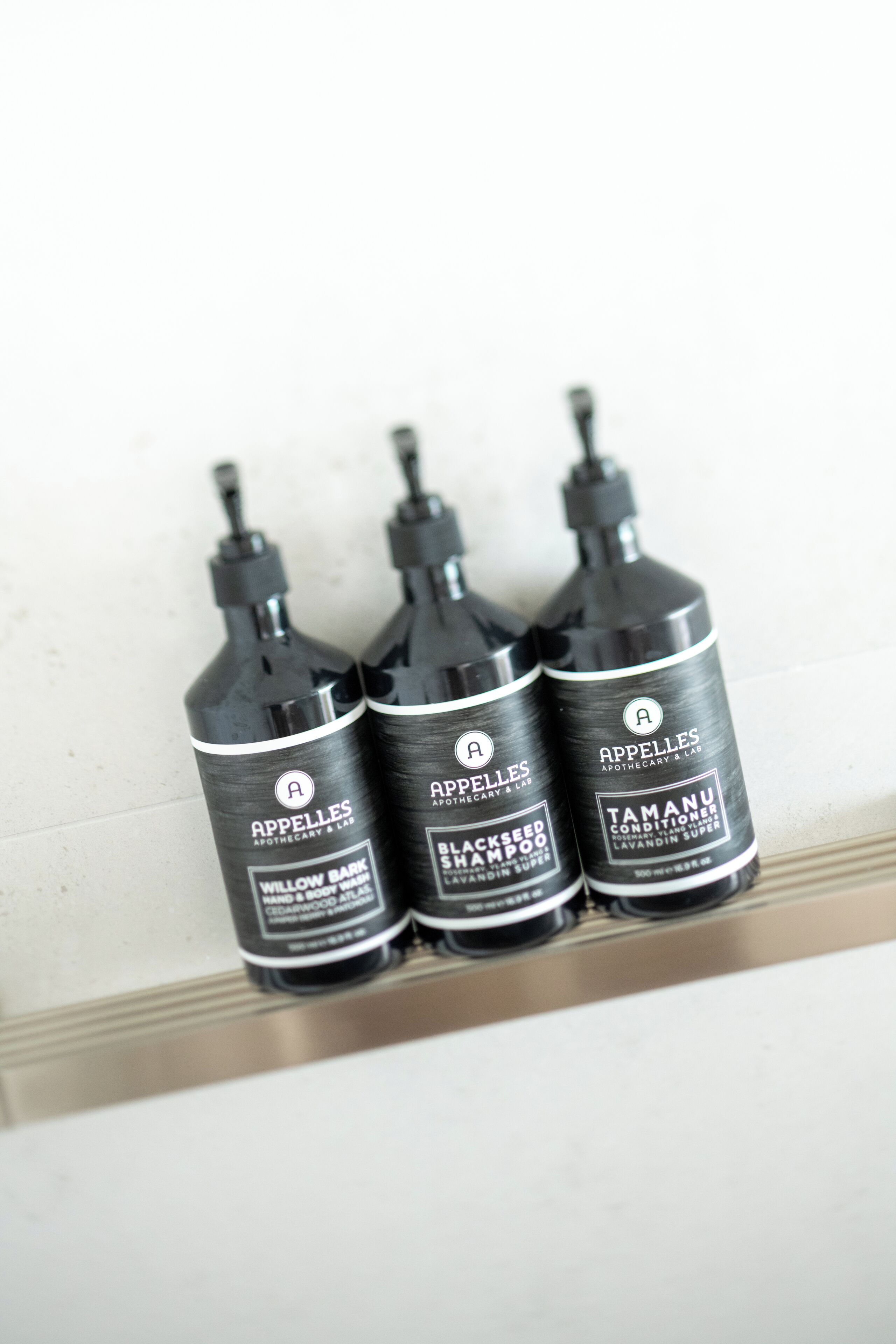 Three black bottles of shampoo on a white shelf.