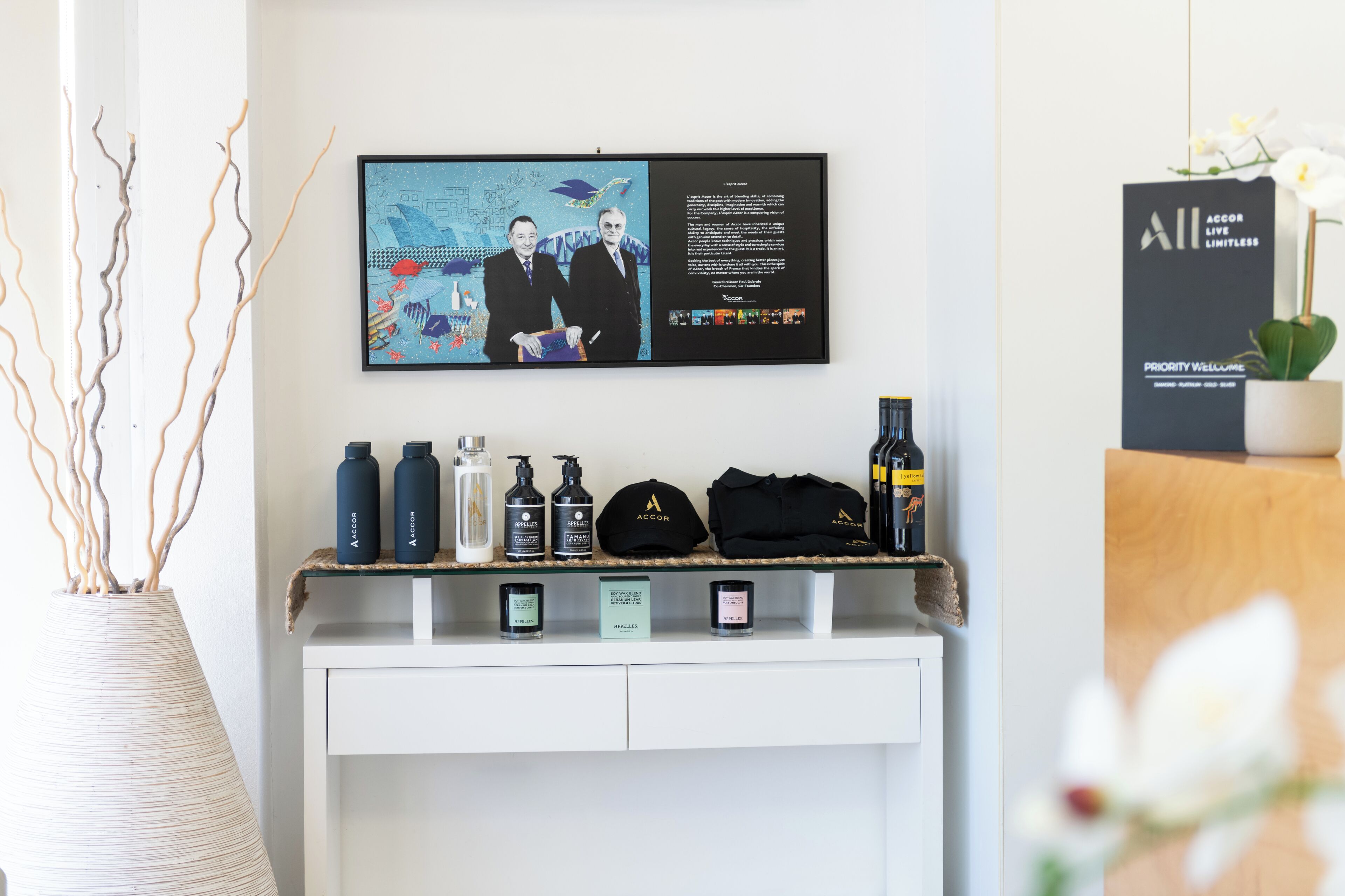 A reception desk with a framed picture, a black bag, and several bottles.