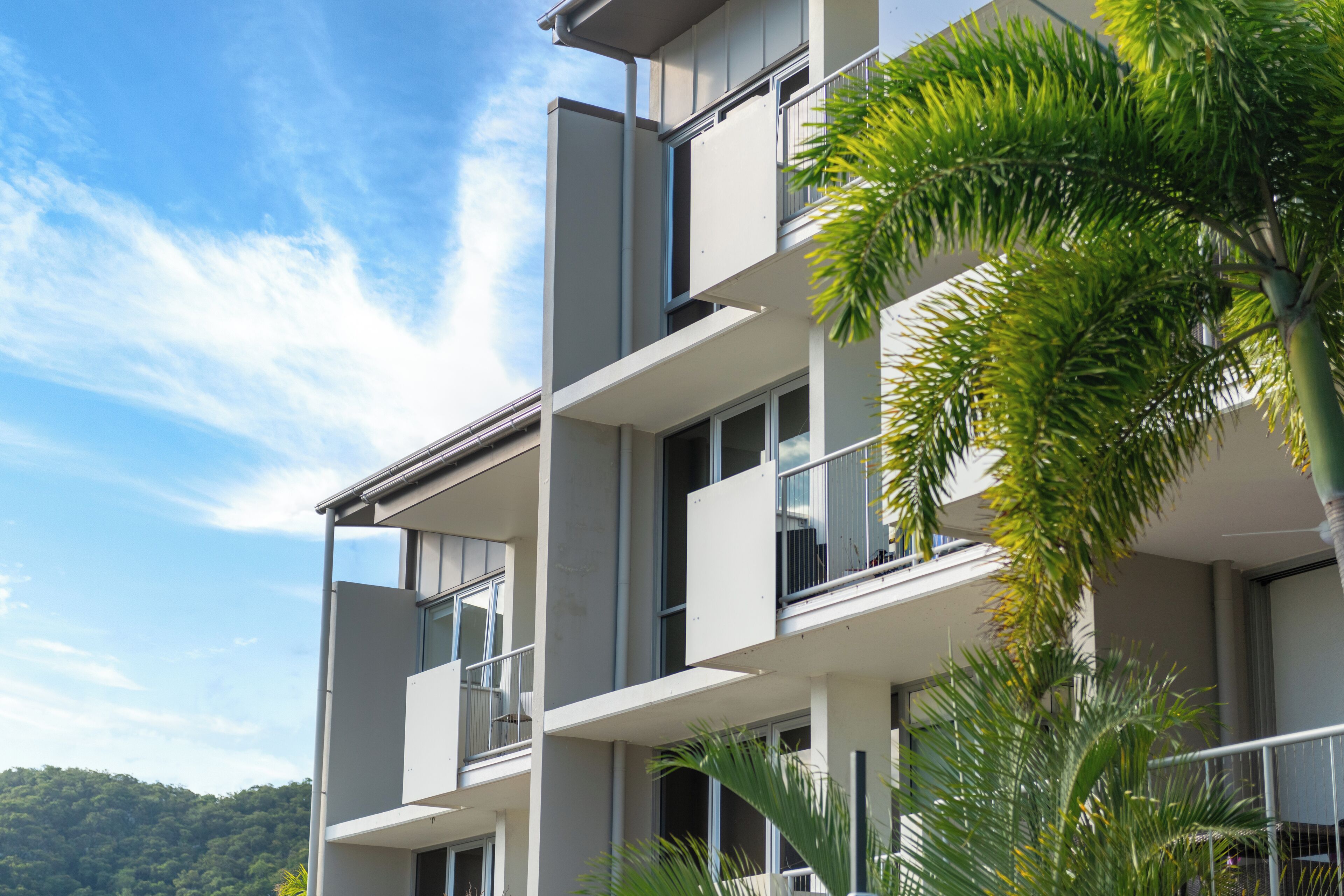 A multi-story building with balconies and large windows, surrounded by greenery.