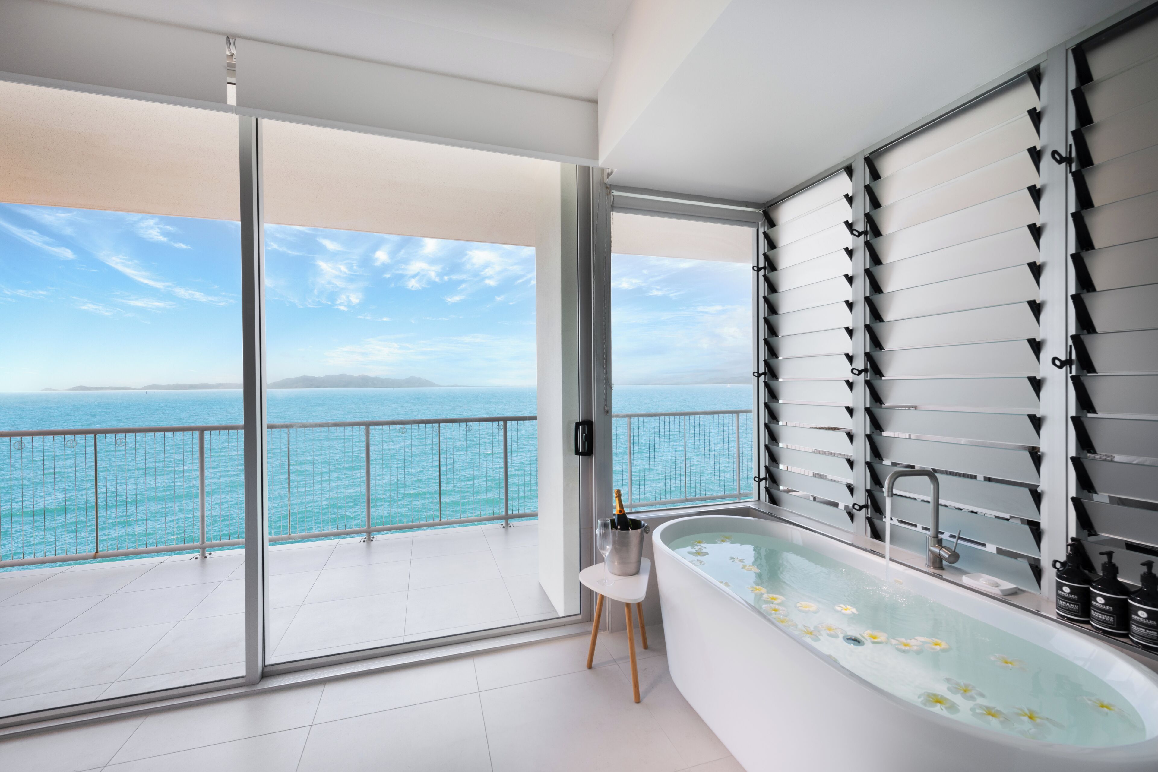 Ein modernes Badezimmer mit einer großen Badewanne und einer Glastür, die auf einen Balkon mit Meerblick führt.