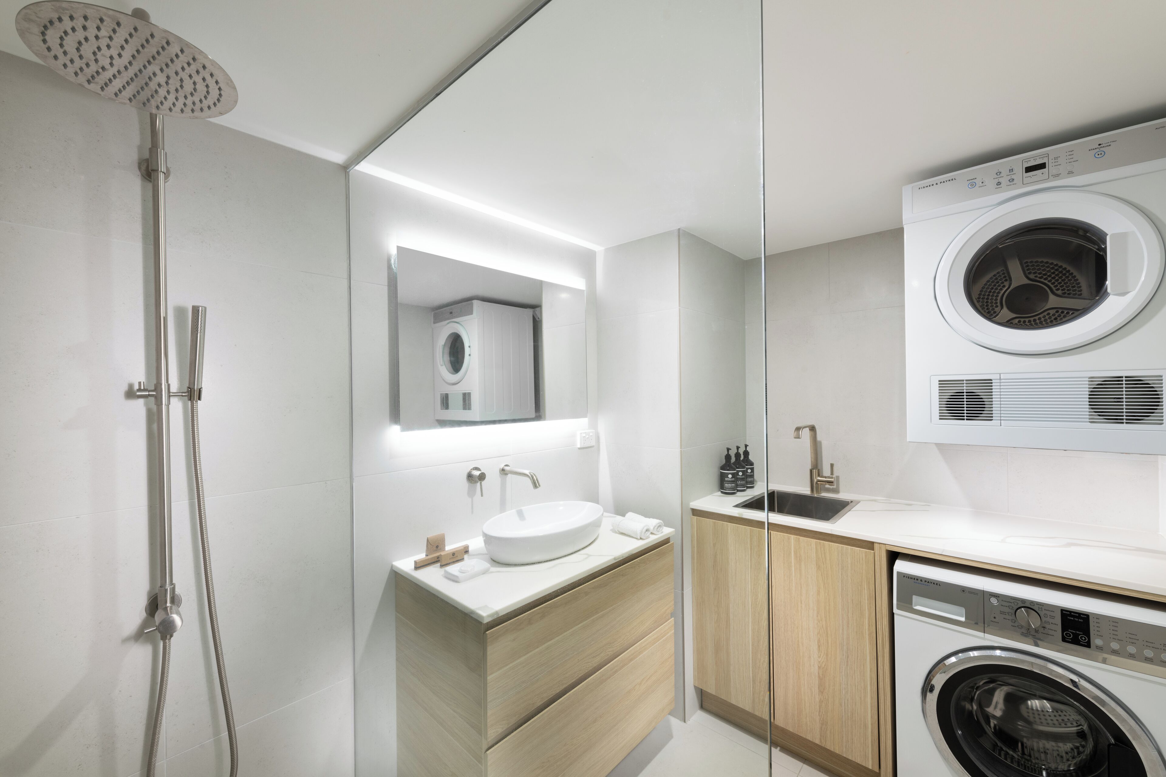 Un baño moderno con ducha integrada, lavamanos con espejo, lavadora y armarios de madera.