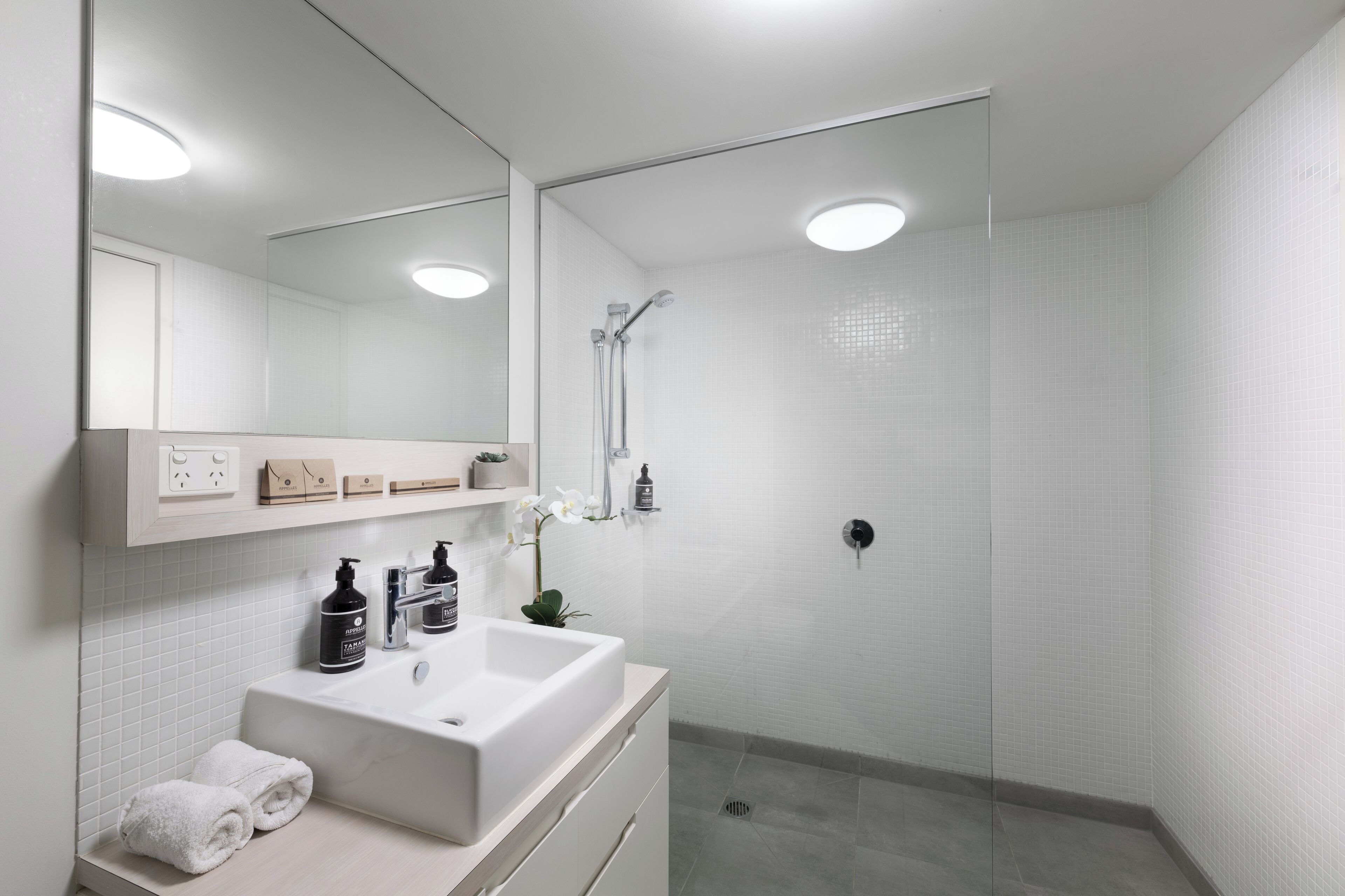 Un baño moderno con un lavamanos, espejo y ducha blancos.