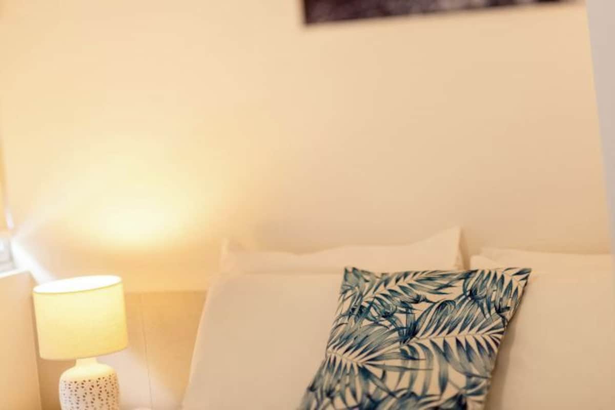 A hotel room with a bed, a nightstand with a lamp, and a wall-mounted painting.