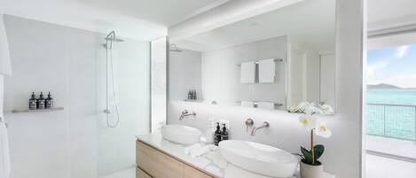 A modern bathroom with a glass-enclosed shower, a large mirror, and a view of the sea.