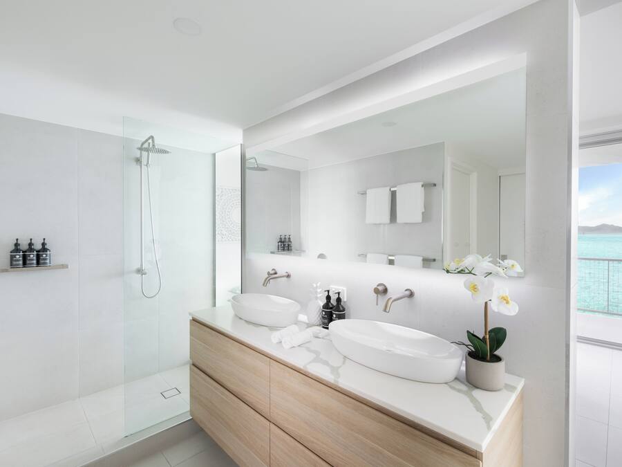 A modern bathroom with a glass-enclosed shower, a large mirror, and a view of the sea.