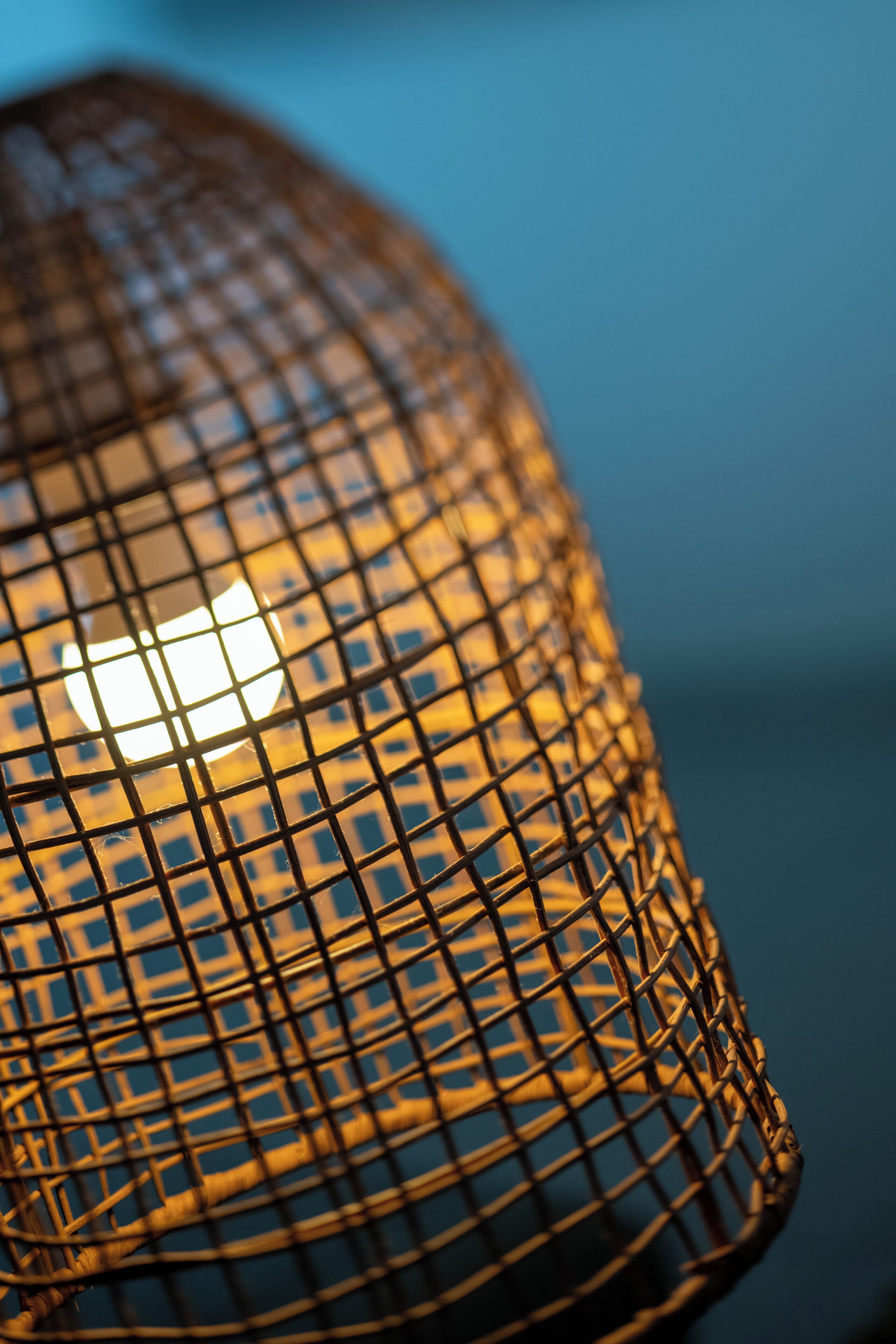 A close-up of a woven metal lamp with a glowing light source behind it.