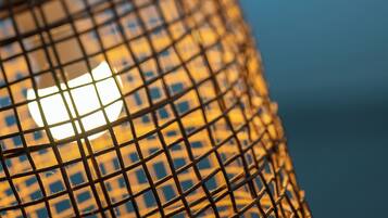 A close-up of a woven metal lamp with a glowing light source behind it.