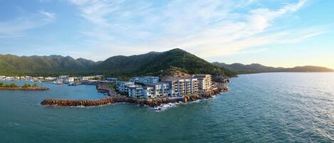 A coastal hotel with multiple buildings, a rocky breakwater, and a mountainous backdrop.