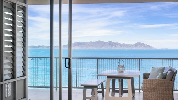 Ein Balkon mit Tisch und Stühlen, mit Blick auf ein Gewässer und entfernte Berge.