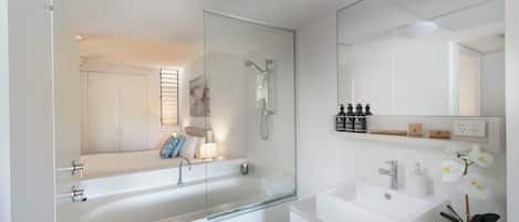 A modern bathroom with a glass-enclosed shower, a large bathtub, a sink, and a mirror.