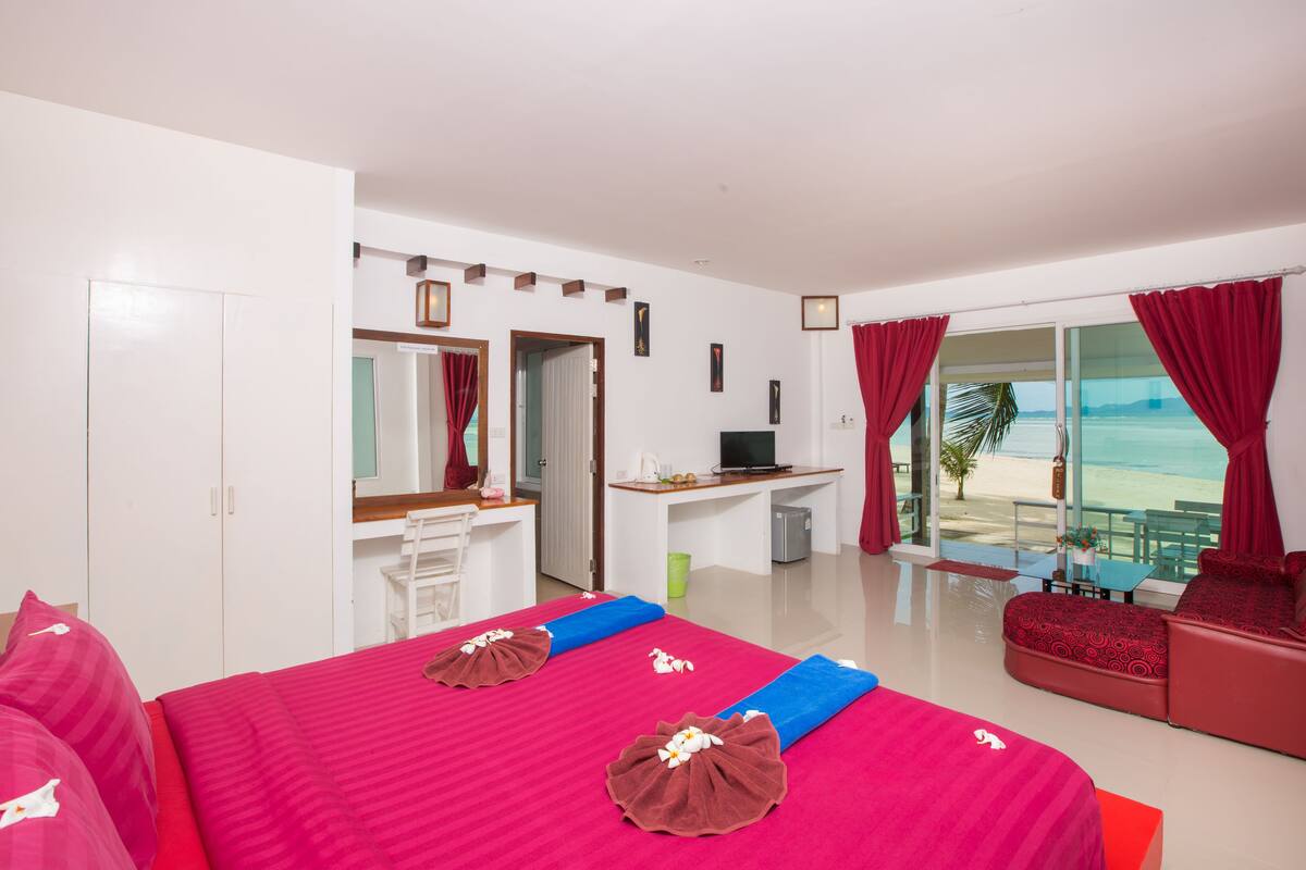 Quarto de hotel com cama, escrivaninha, televisão e varanda com vista para a praia.