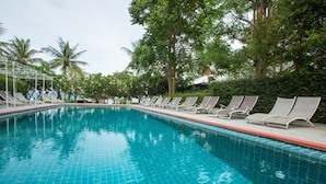 Uma piscina com bordas azulejadas, rodeada por espreguiçadeiras e palmeiras.