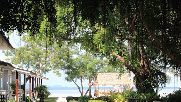 Um hotel à beira-mar com área de estar coberta ao ar livre, um caminho que leva à praia e vegetação exuberante.
