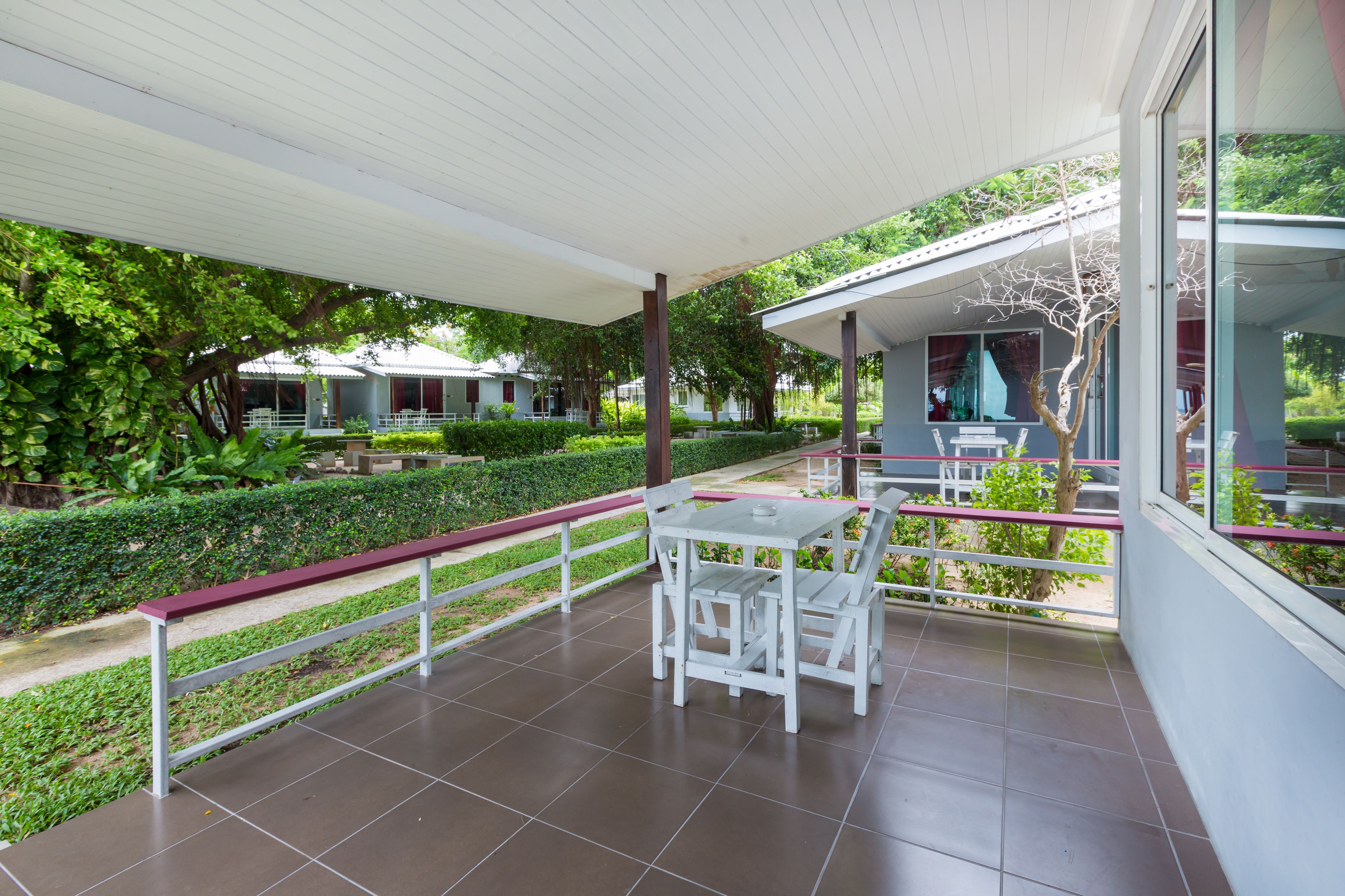 A covered outdoor patio with a white table and chairs, surrounded by greenery and a white railing.