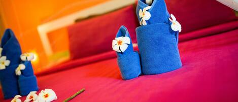 A bed with red bedding and blue slippers adorned with white flowers.