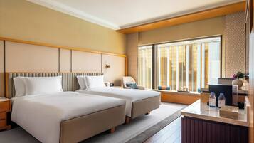 A hotel room with two beds, a desk, and a large window.