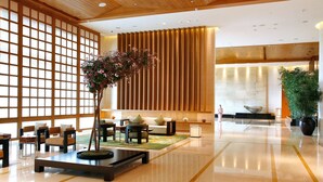 Un hall espacioso con un separador de madera tradicional, una mesa de recepción, zona de estar y una planta grande en maceta.