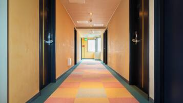 Pasillo de hotel con una alfombra colorida, puertas a ambos lados y una señal de salida visible.