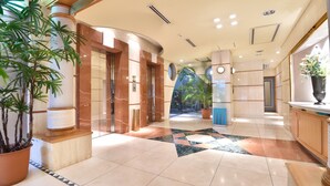 Een hotel lobby met marmeren vloeren, een grote potplant en uitzicht op een tropische tuin door de glazen deuren.