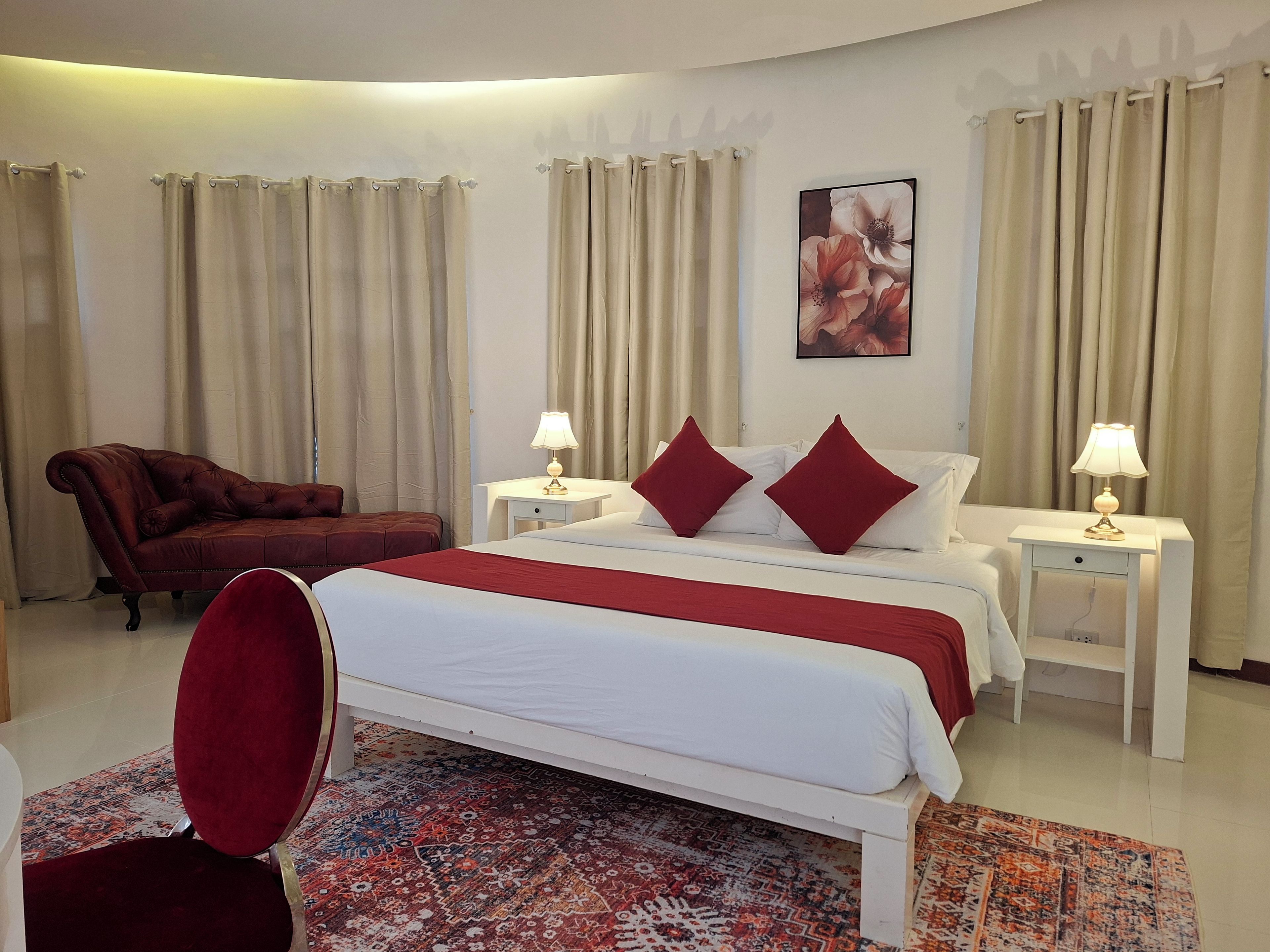 A hotel room with a bed, two bedside tables with lamps, a red armchair, and a patterned rug.