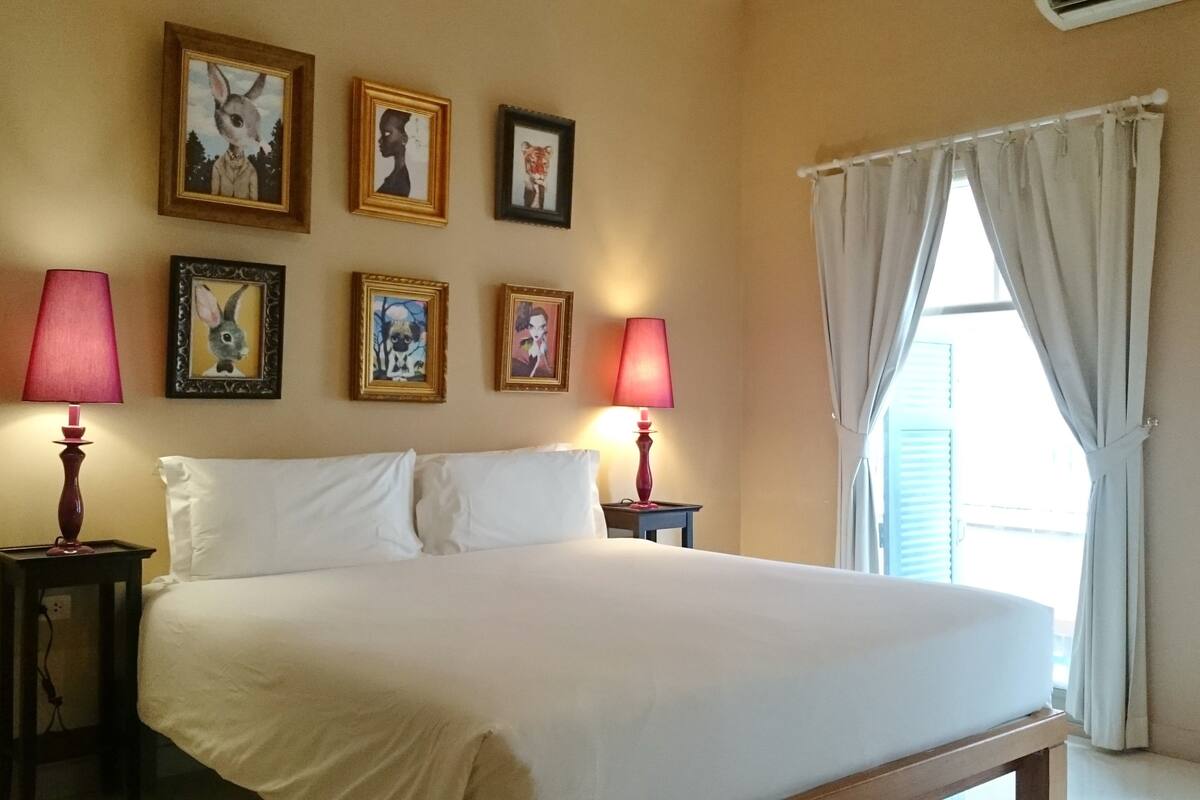 A hotel room with a large bed, two bedside lamps, and a window with curtains.