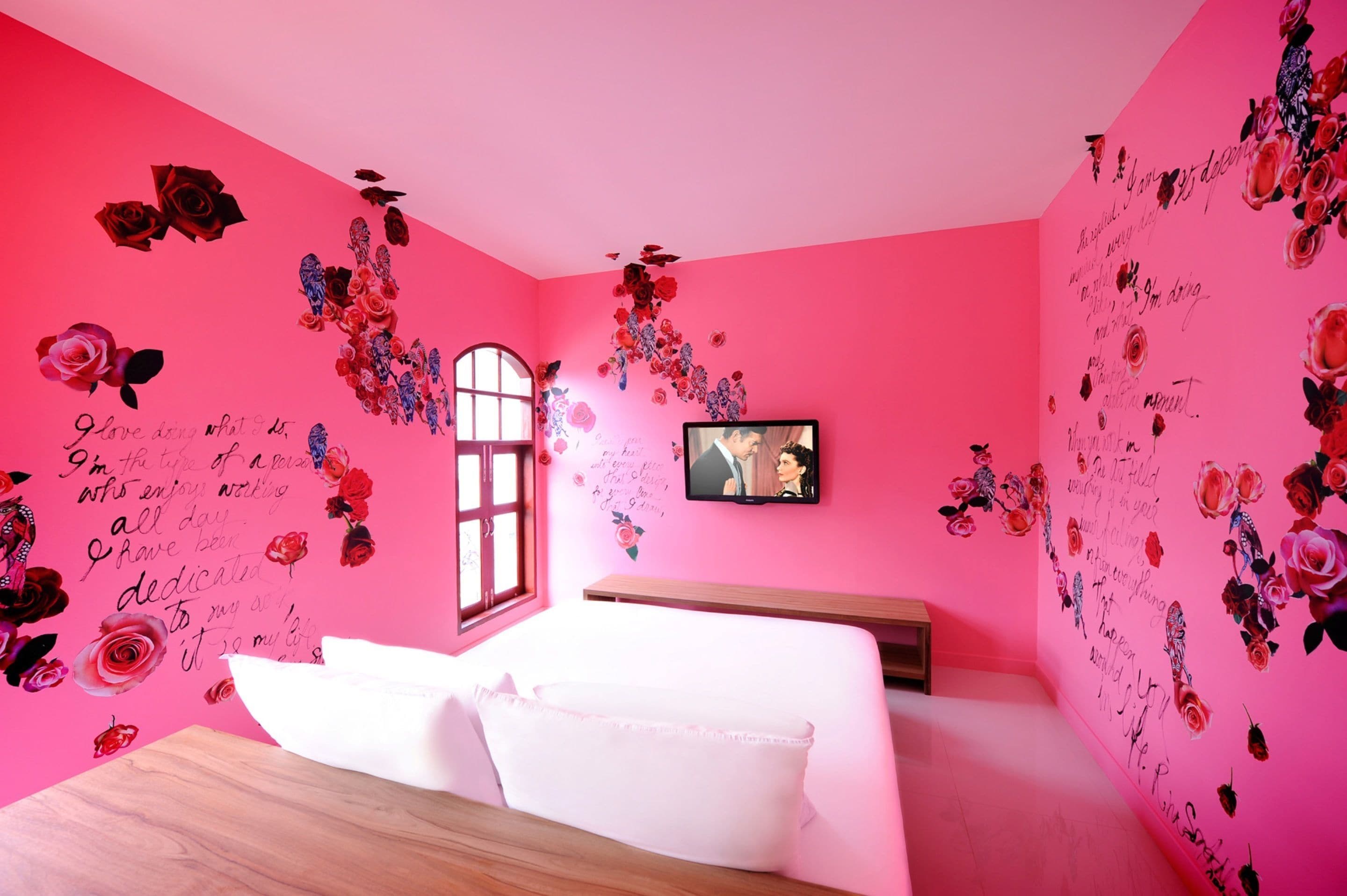 A pink room with floral decals, a bed, a TV, and a window.