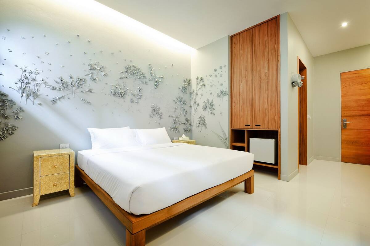 A modern bedroom with a wooden bed, a nightstand, a wardrobe, and a wall with floral decals.