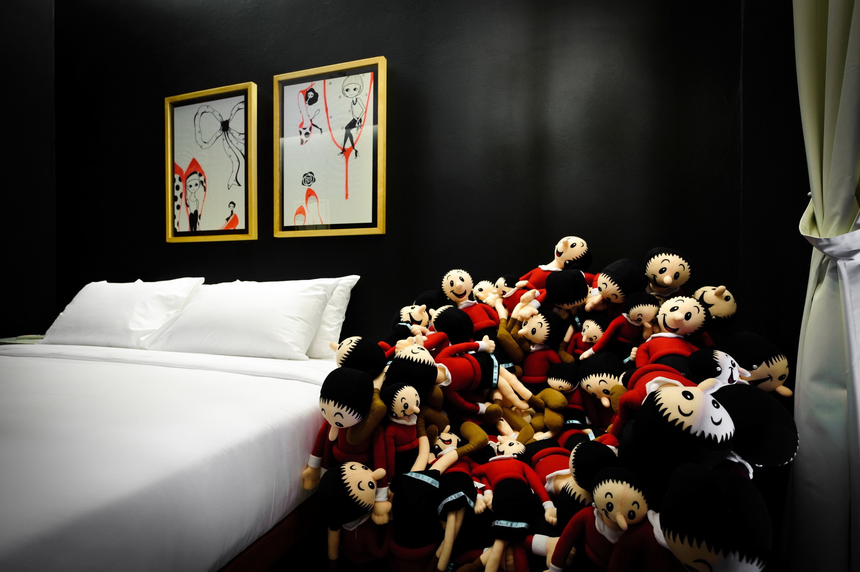 A bedroom with a bed, two framed artworks on the wall, and a pile of plush toys on the bed.