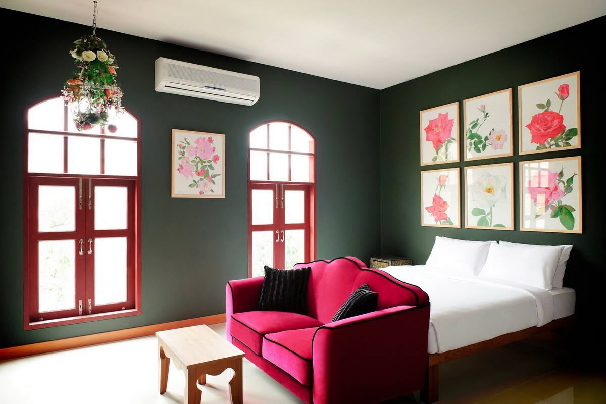 A room with a red sofa, a white bed, and multiple windows with red frames.
